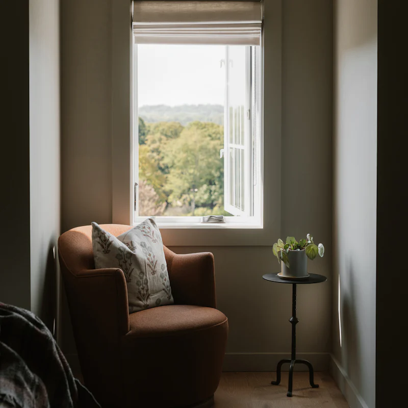 A soft armchair beside an open window looking out on green trees