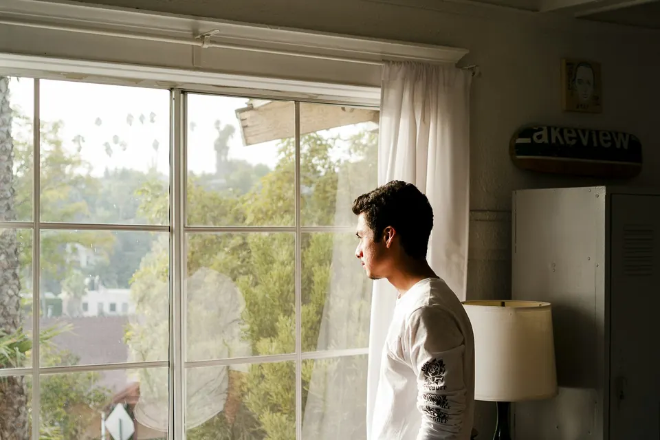 A man standing by a window, looking out, deep in thought