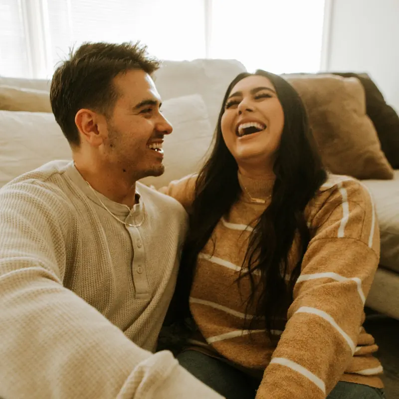 A couple laughing together on a sofa, holding hands